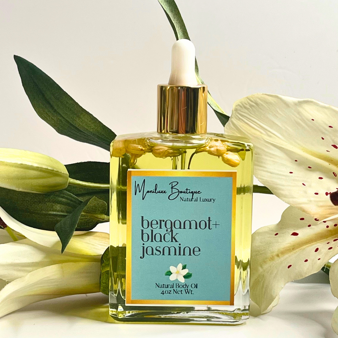 Square glass bottle filled with bergamot and black jasmine scented body oil. Includes a glass oil dropper. Bottle posed against a background of white lilies.