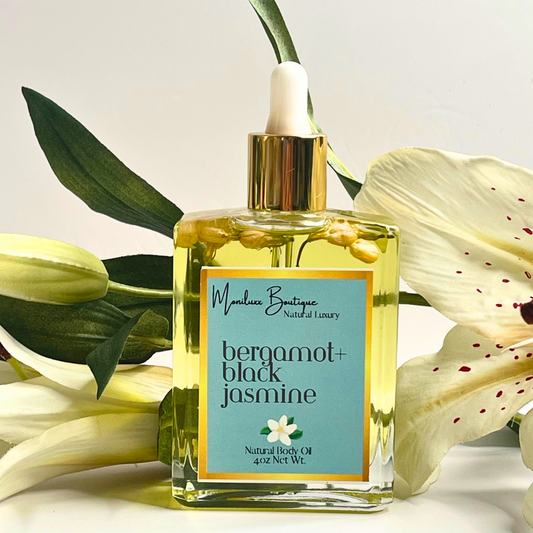 Square glass bottle filled with bergamot and black jasmine scented body oil. Includes a glass oil dropper. Bottle posed against a background of white lilies.